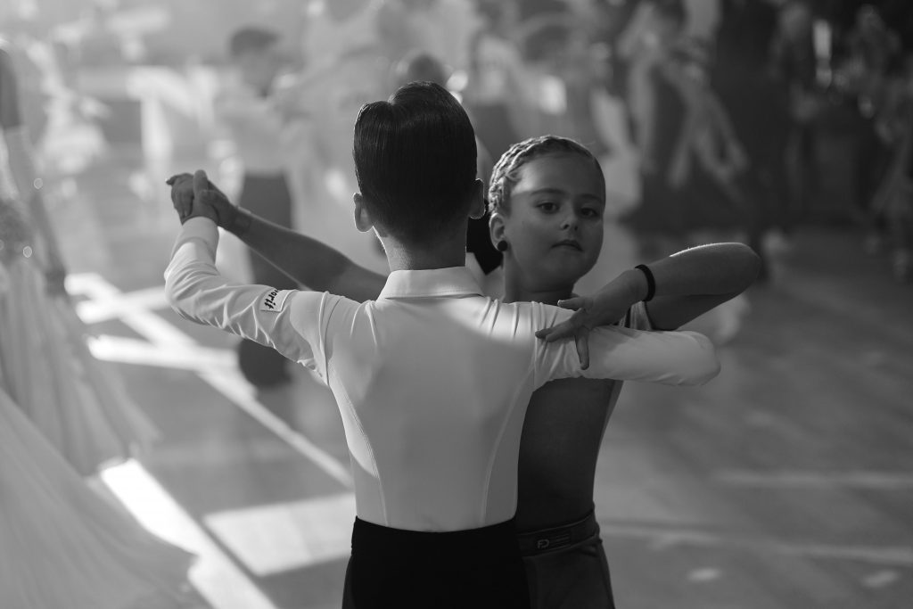 Young dancers performing ballroom dance in a black and white setting.